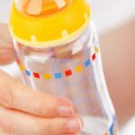 Close up of pregnant woman's hand holding a baby bottle with yellow cap