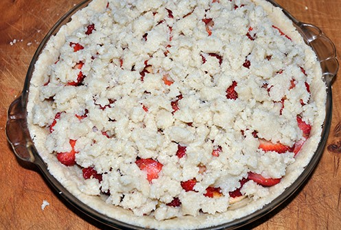 Crumble topping sprinkled over apple and strawberry pie filling in pie pan