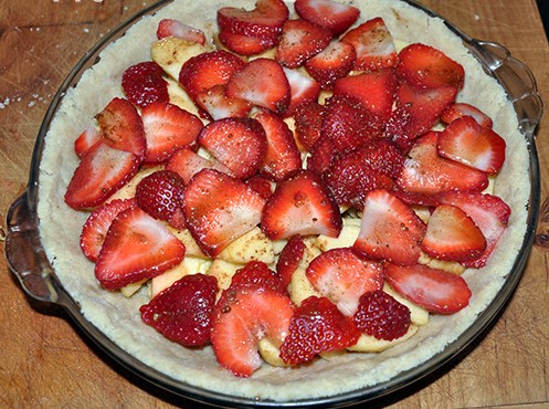 Apples and strawberries layered in a gluten free pie crust in clear pie pan on cutting board
