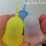 Three Sckooncup menstrual cups in a hand with color options below