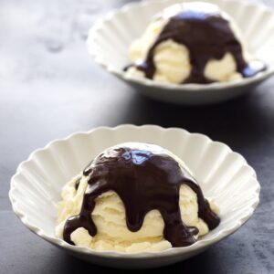 Two bowls of Magic Shell topped vanilla ice cream in white bowls on a dark counter