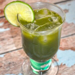 Matcha mojito cocktail garnished with lime wedge on worn wood table with blue paint remnant