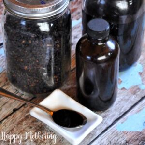 Mason jar of elderberries and a jar of homemadeelderberry syrup with some poured on a spoon