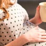 Pregnant woman drinking tea and resting her hand on her belly