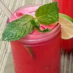 Close up of watermelon agua fresca served in pint sized mason jar with sprig of mint and slice of lime
