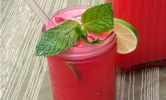 Close up of watermelon agua fresca served in pint sized mason jar with sprig of mint and slice of lime