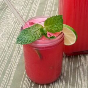 Pint sized mason jar filled with homemade watermelon agua fresca next to full pitcher on table with green tablecloth