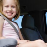 Close up of smiling girl in back seat of car sitting in booster seat with seat belt