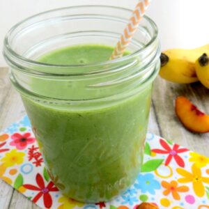 Green smoothie with peaches and pineapple in a mason jar with yellow striped paper straw