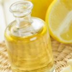 Close up of bottle of lemon essential oil and half a lemon on a mat