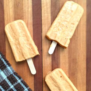 Two homemade pumpkin yogurt popsicles on a cutting board with a dish towel