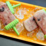 Four creamy cherry fruit popsicles on ice on a long rectangular orange serving tray