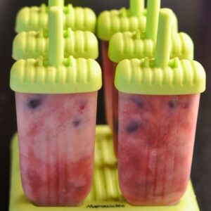 Six homemade cherries and cream fruit popsicles still in their mold after being frozen