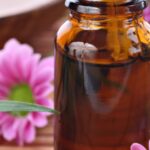 Closeup of amber essential oil bottle on table with fresh pink flowers