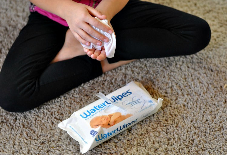 Zoe wiping her hands with Waterwipes while sitting on the carpet