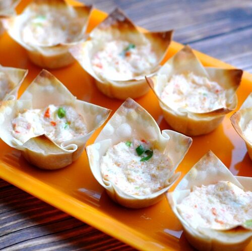 Mini crab tartlets made with wonton wrappers on orange serving platter on wood table