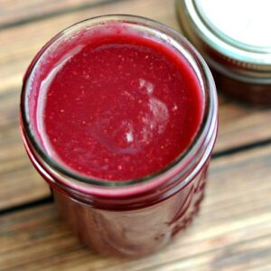 Overhead view of 8 ounce glass mason jar of pomegranate syrup next to a smaller jar on a wood table