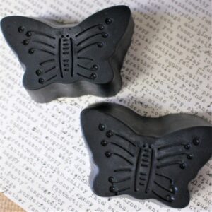 Two activated charcoal soap bars shaped like butterflies laying on newsprint