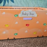 Side view of orange baby box on floor next to bed