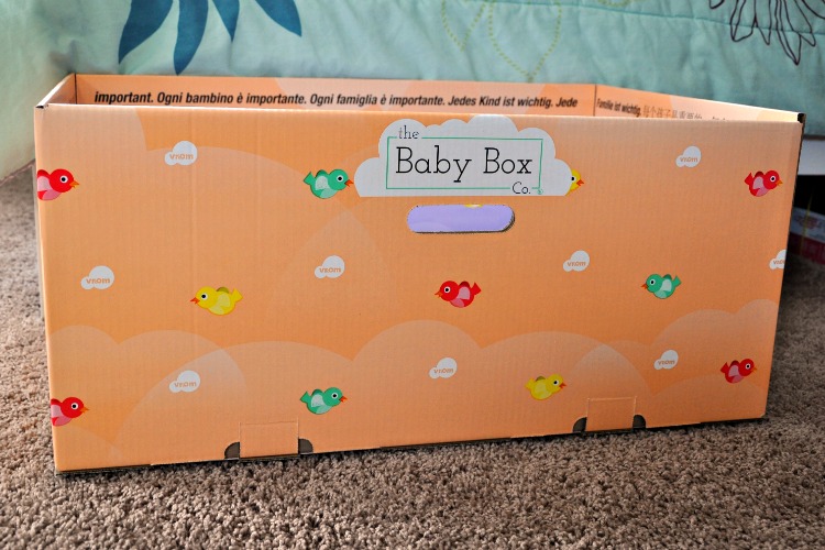 Side view of orange baby box on floor next to bed