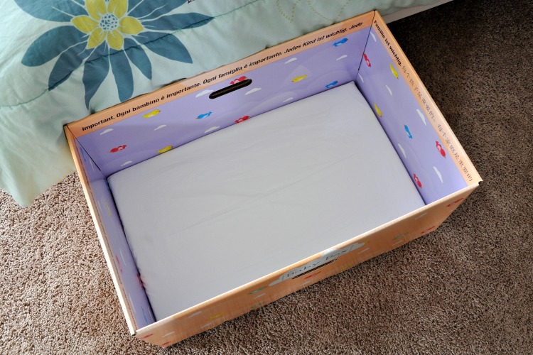 Overhead view of mattress inside baby box on floor next to bed