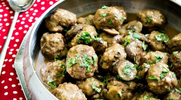 Silver bowl of Salisbury Meatballs with mushrooms on a red and white polka dot place mat with silver spoon