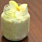 Matcha Overnight oats in a jar topped with apple slices on a table with extra apple slices