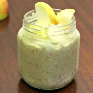 Close up of matcha overnight oats in a jar topped with apples on a wood table