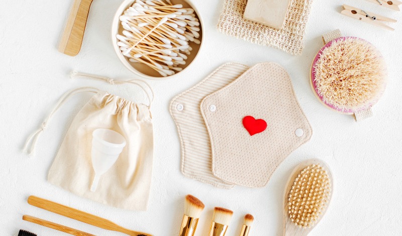 White table covered in cloth pads, menstrual cup, dry brusk, q-tips and other natural beauty items.