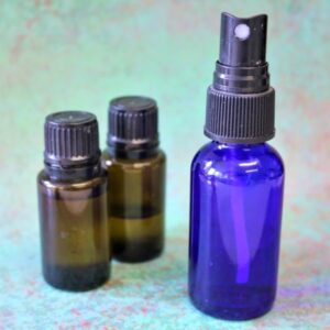 One blue glass spray bottle and two bottles of essential oil on a colorful background