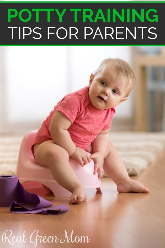 Little girl in pink onesie sitting on a pink potty chair in her living room on wood floors