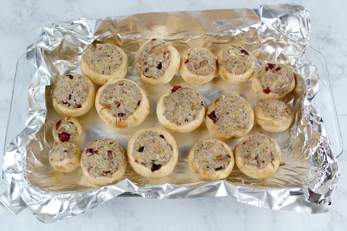 Sausage stuffing pressed into mushrooms on a foil lined pan