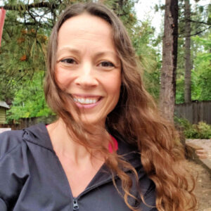 Chrystal Johnson with wavy hair blowing in the wind with the forest in the background