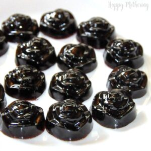 A dozen homemade elderberry gummies shaped like little roses on white plate.