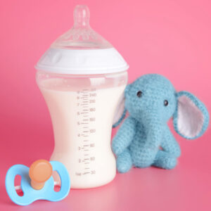 Baby bottle, pacifier and stuffed elephant on pink background.